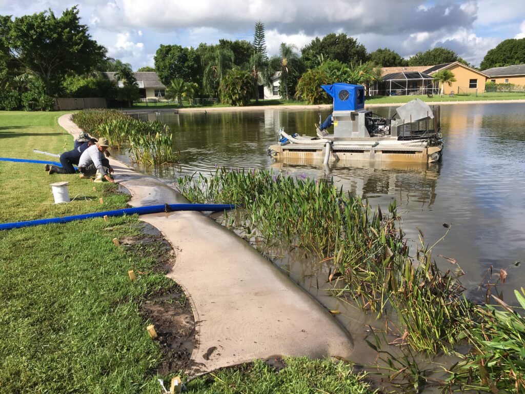 Crew installing bioengineered living shoreline with native plantings along a residential pond, with a work boat in the water