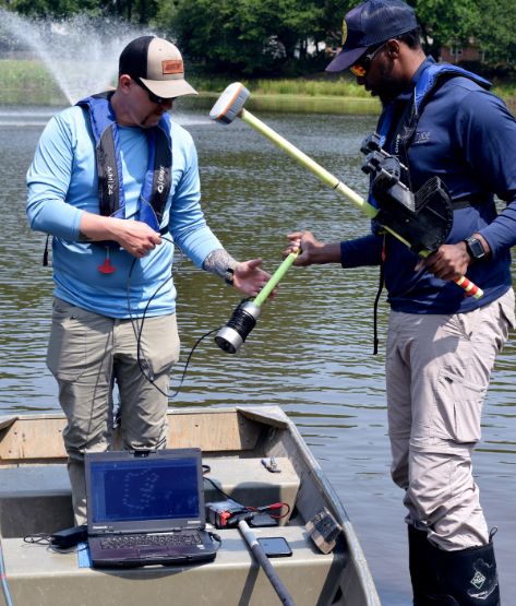two aquatic experts setting up to preform a bathymetry study of the community lake behind them